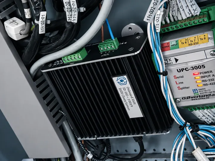 Close-up of an asset-tagged DIDI Onboard Unit wired beside a UPC-3005 NMEA serial line splitter in a ship equipment cabinet